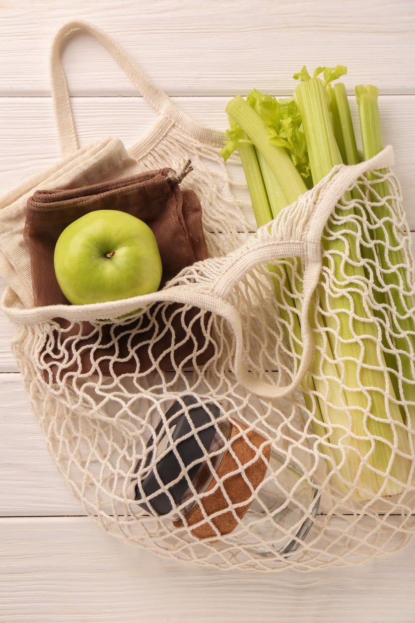 Net bag with different items on white wooden table, top view charity giving