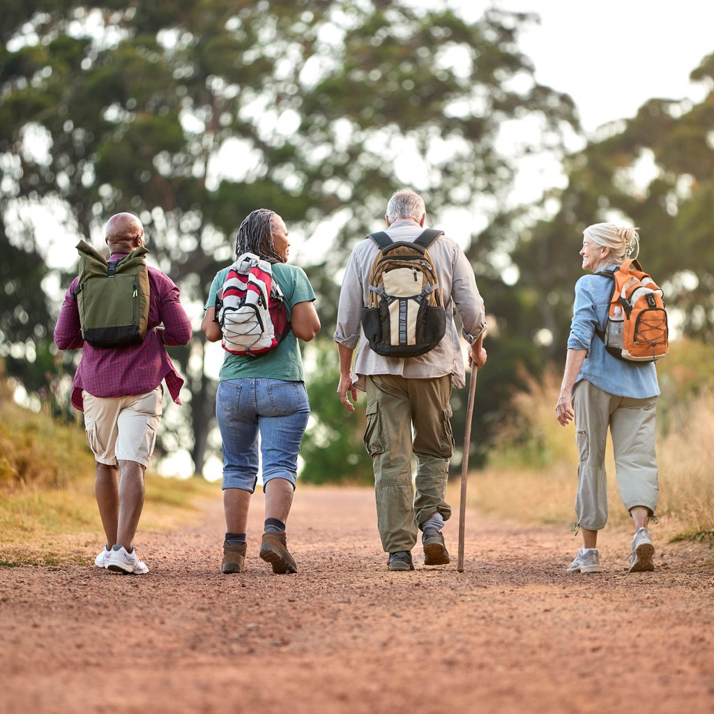 Rear view of active senior friends enjoying hiking through countryside walking along track fundraising